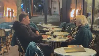 paris-couple-sips-coffee-and-drinks-amid-violent-protests-and-flames-outside-cafe-video